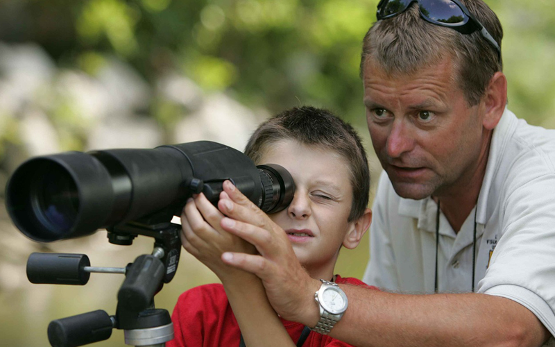 a child using a spotting scope with his father